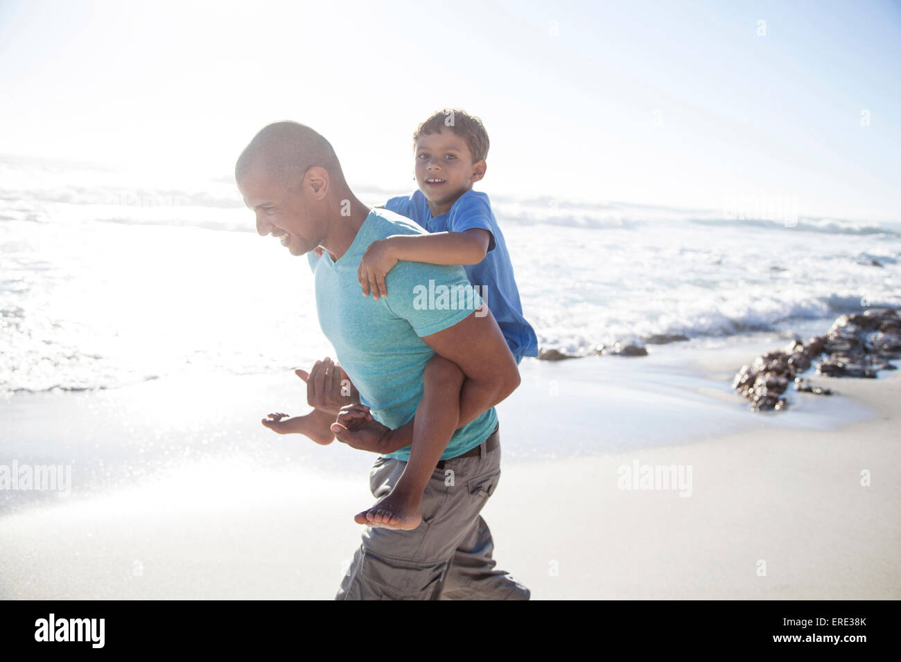 Mixed race father carrying son piggyback on beach Stock Photo