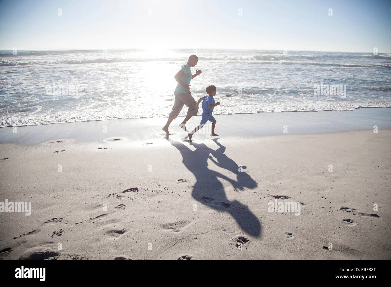 Mixed race father and son running on beach Stock Photo