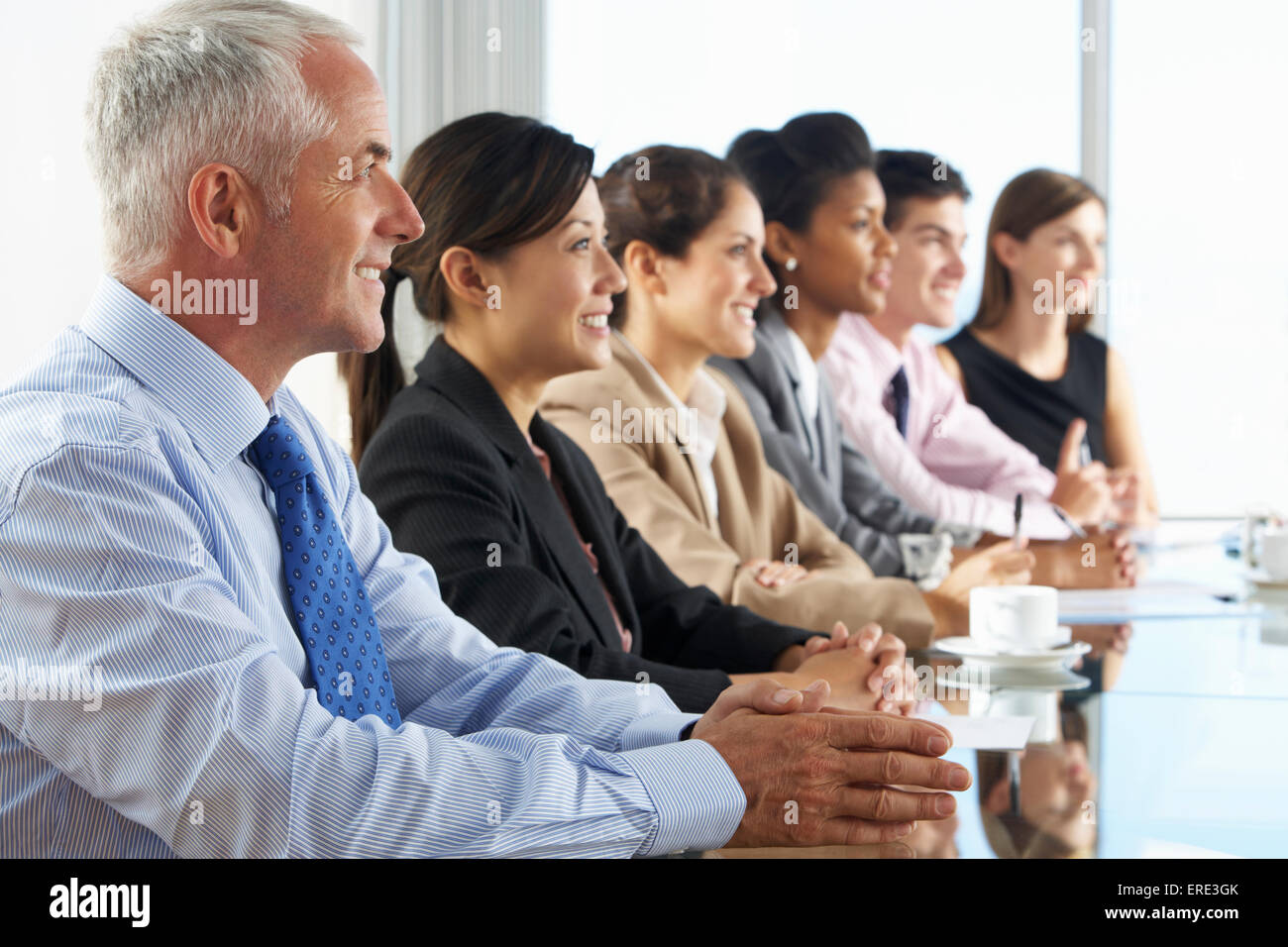 Line Of Business People Listening To Presentation Seated At Glass Boardroom Table Stock Photo