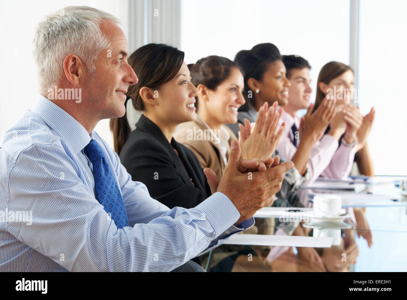 Line Of Business People Listening To Presentation Seated At Glass Boardroom Table Stock Photo
