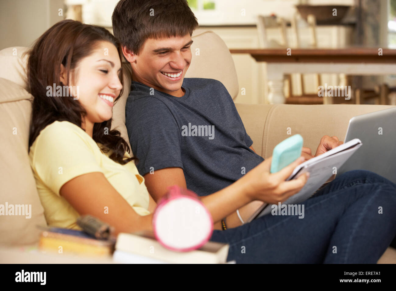 Teenage Boy And Girl Sitting On Sofa At Home Doing Homework Using ...