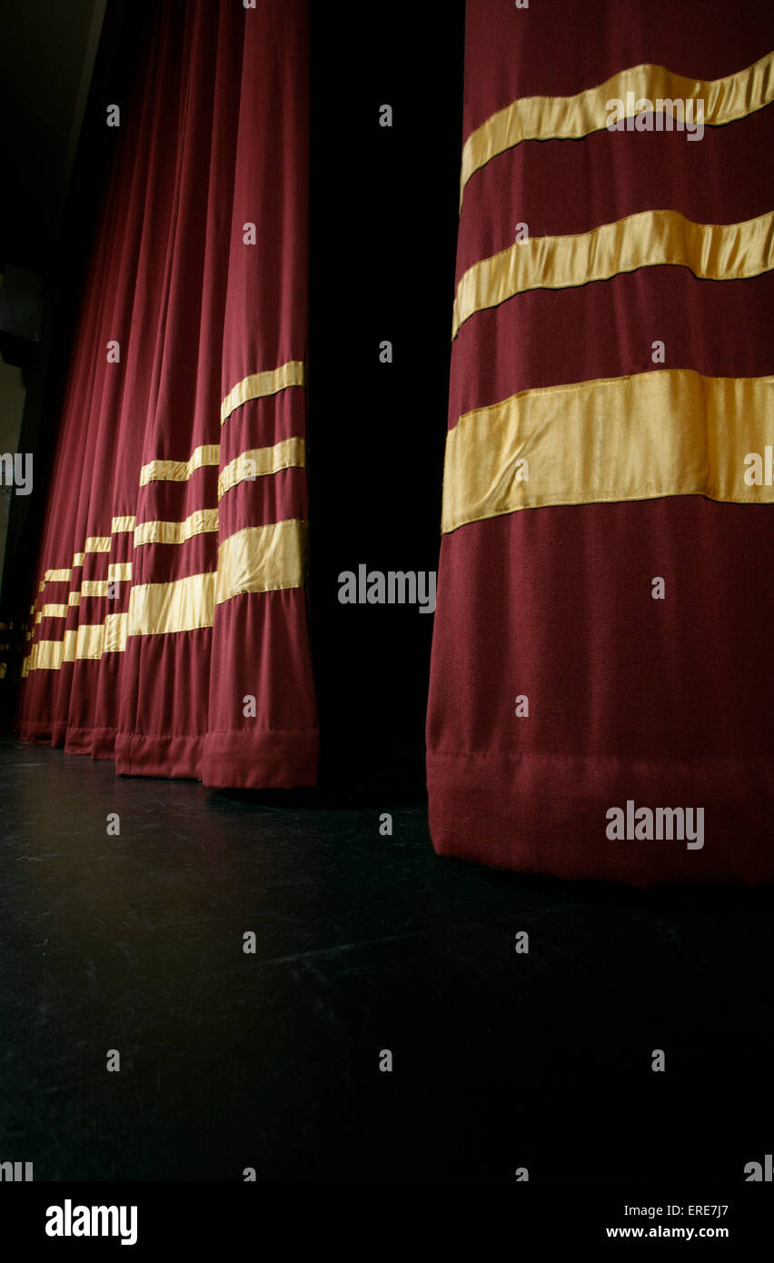 Red stage curtains with gold stripes, partially open to reveal stage Stock Photo
