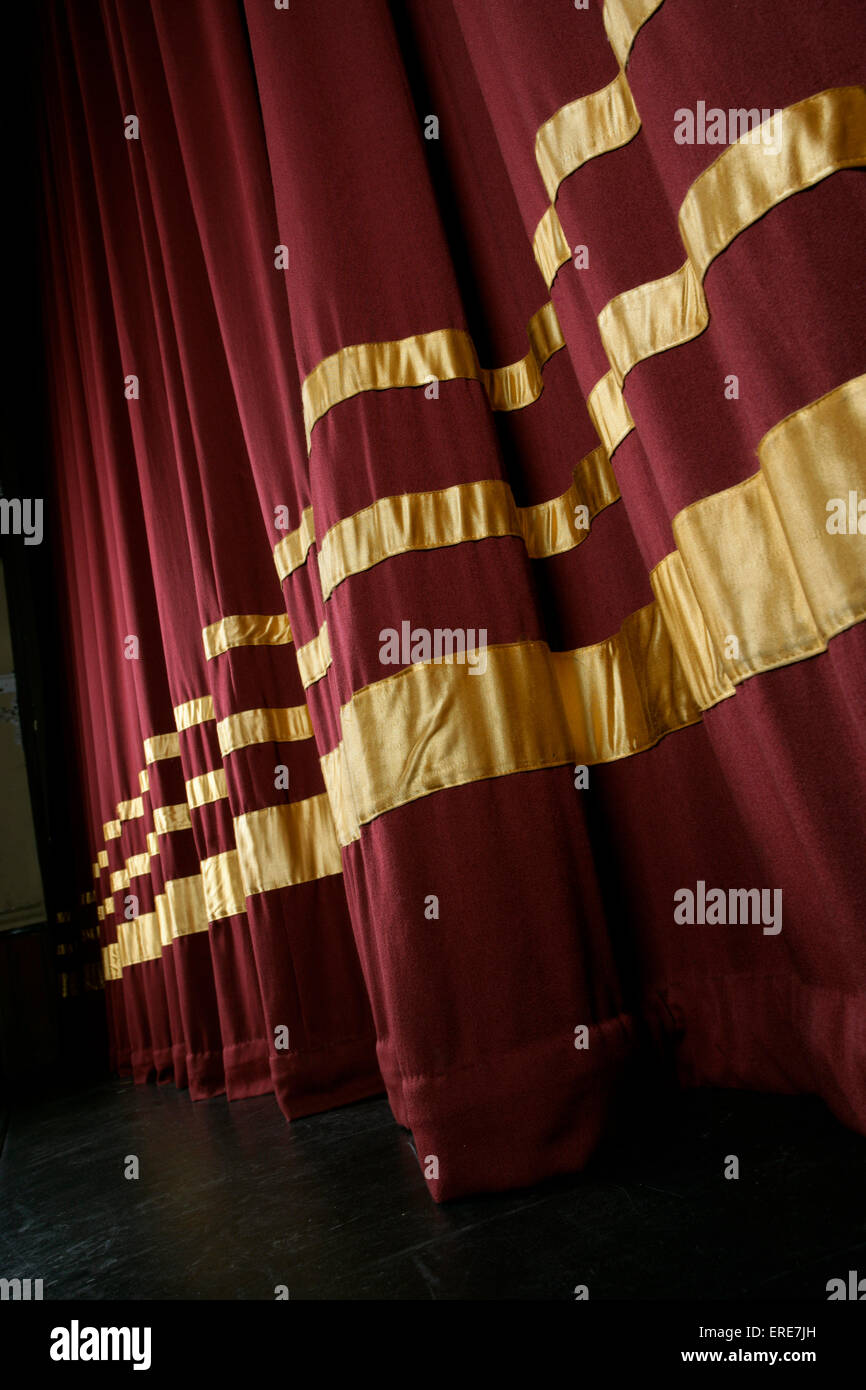 Red stage curtains with gold stripes, partially open to reveal stage Stock Photo