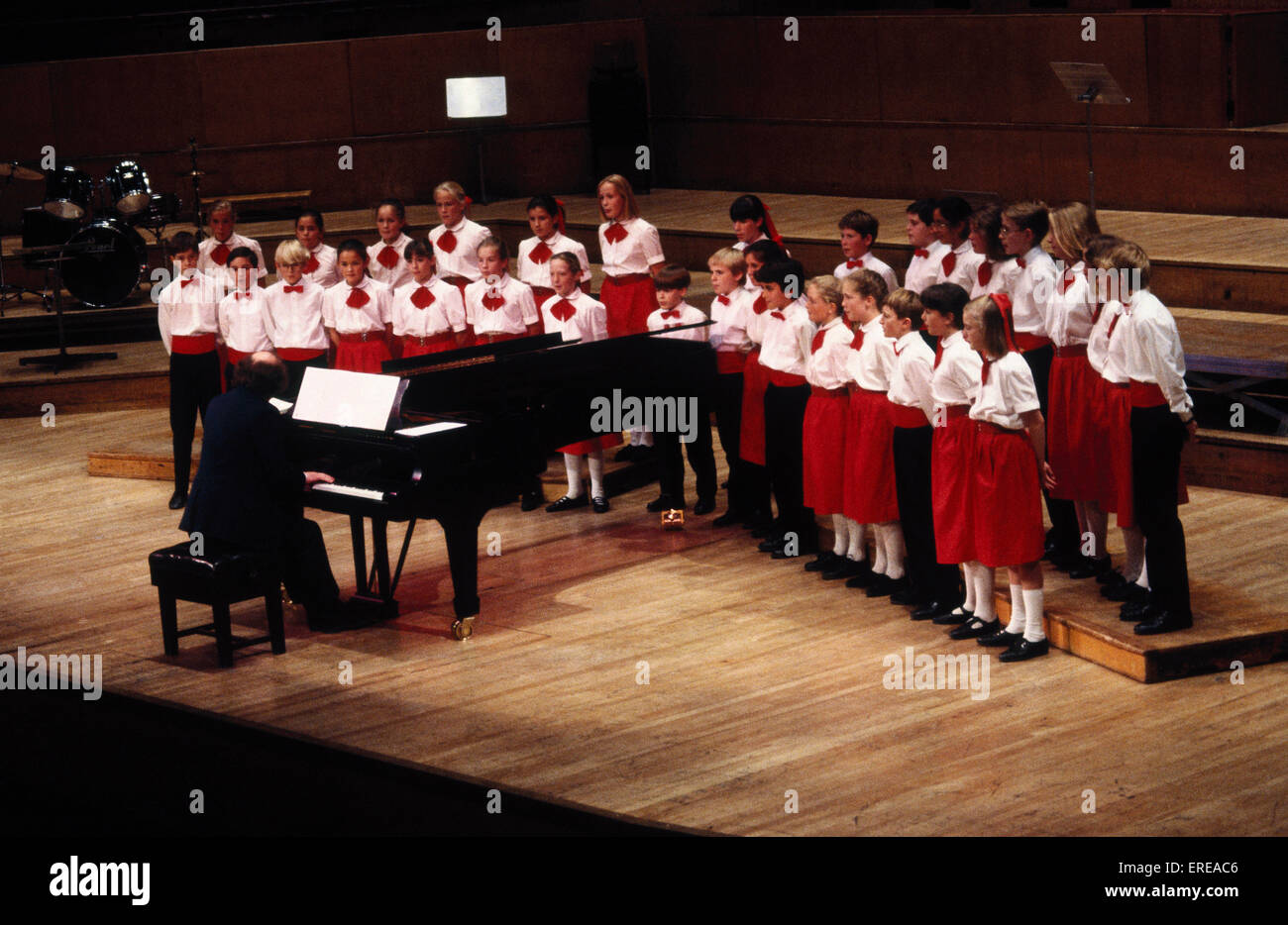 School Children's choir singing, conducted from the piano. Wearing red