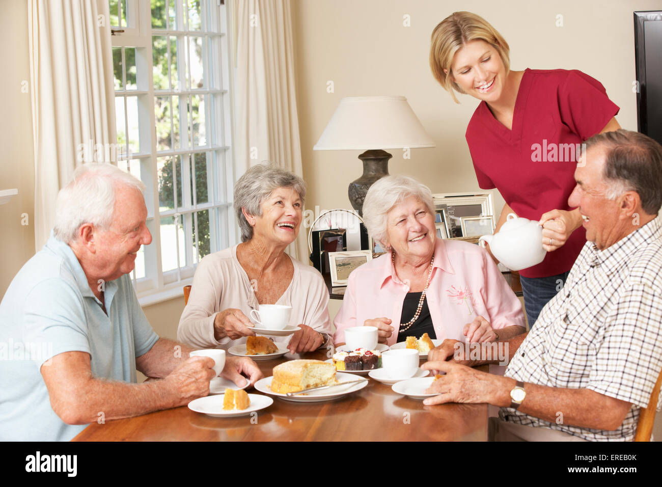Group Of Senior Couples Enjoying Afternoon Tea Together At Home With Home Help Stock Photo