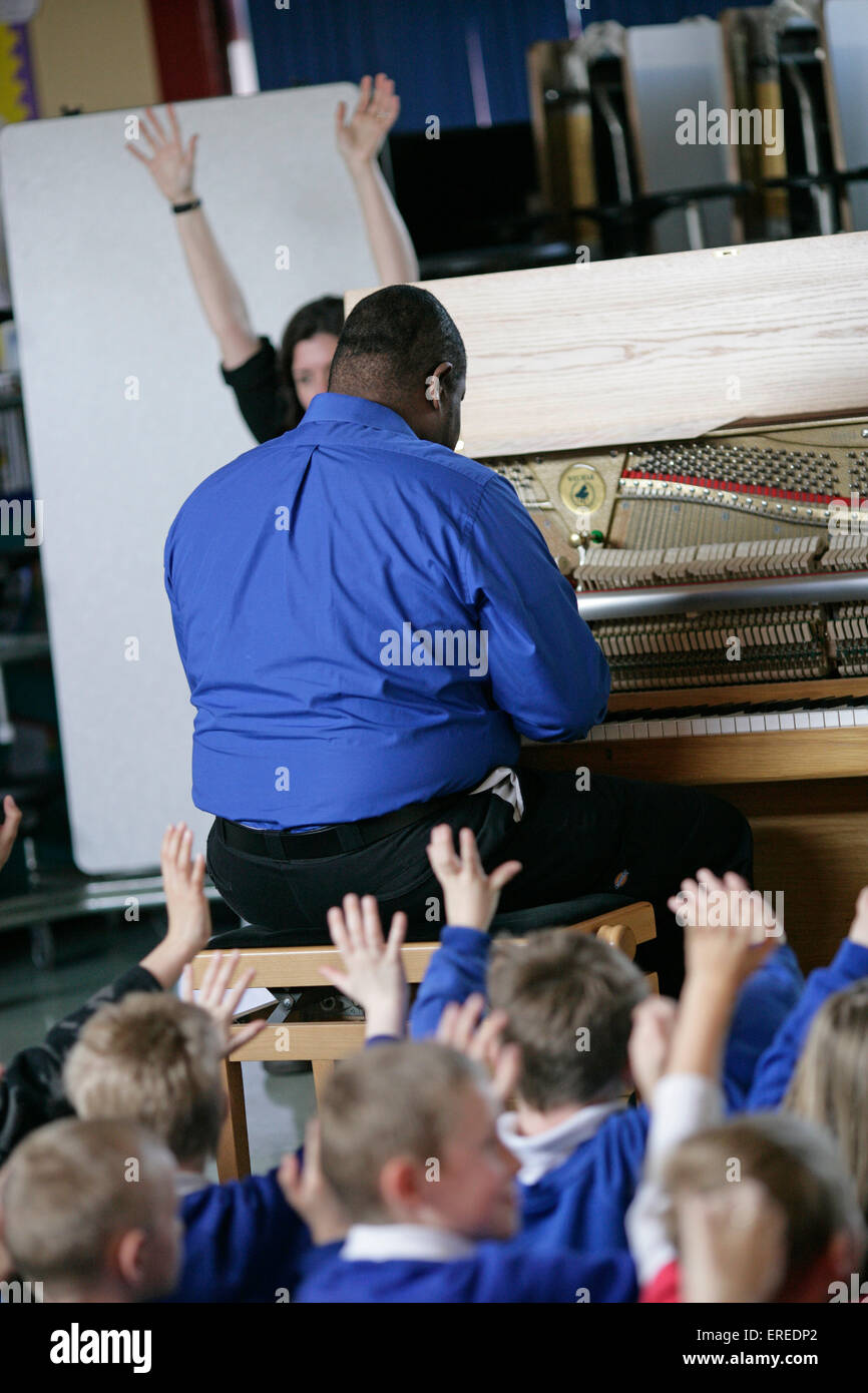 Music workshop in a school with a piano player playing to a class of school children. Stock Photo