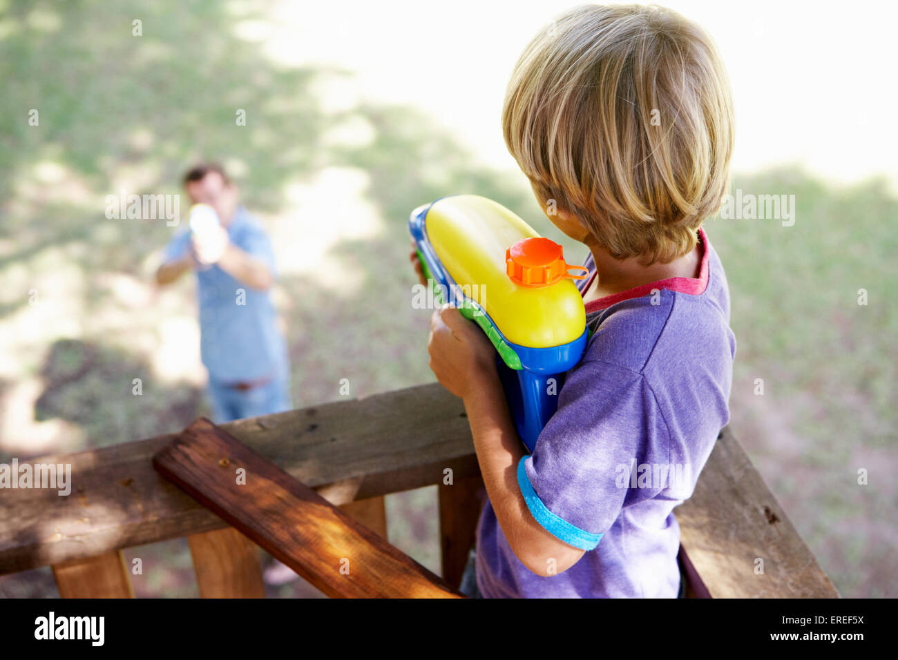 Father And Son Having Water Pistol Fight In Tree House Stock Photo