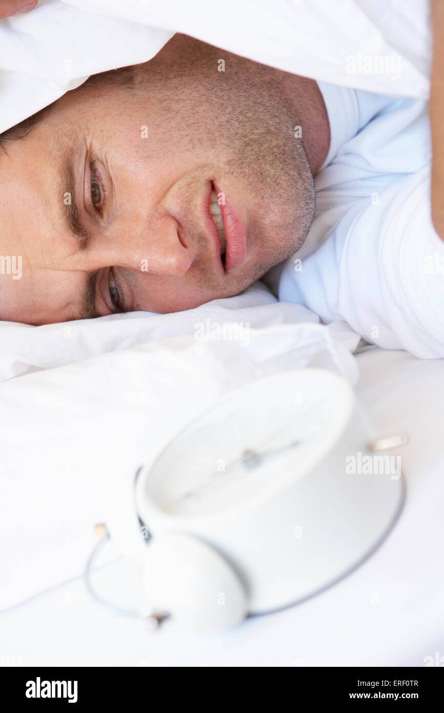 Grumpy Man In Bed Turning Off Alarm Clock Stock Photo