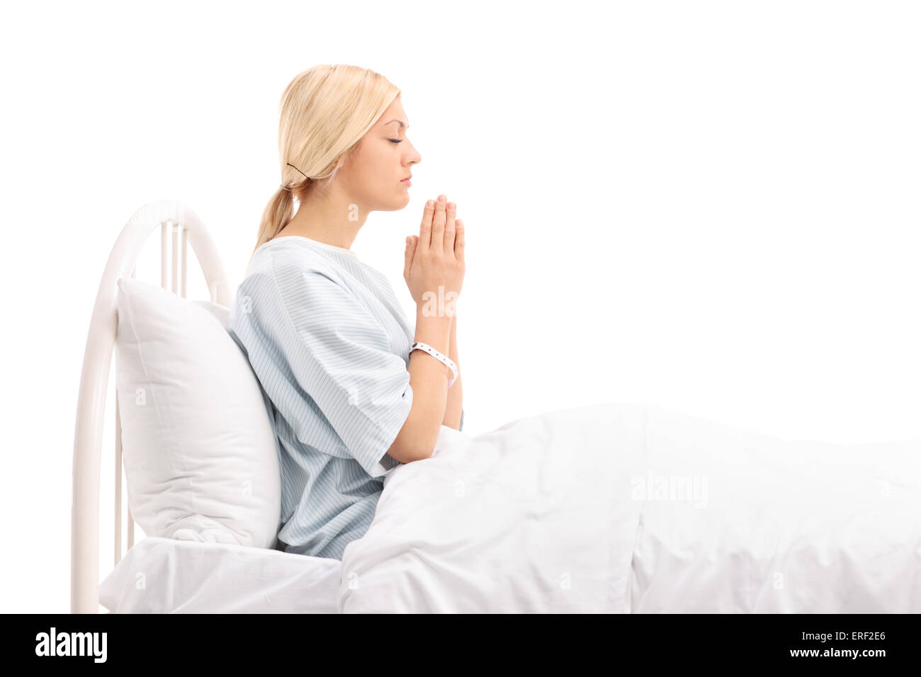 Young female patient lying in a hospital bed and praying to god isolated on white background Stock Photo