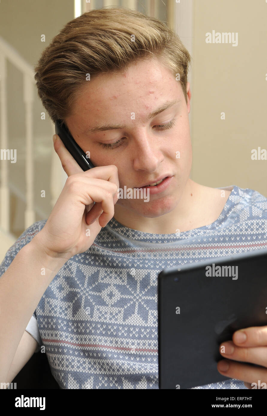 Teenage boy talking on his mobile phone whilst viewing his tablet Stock Photo