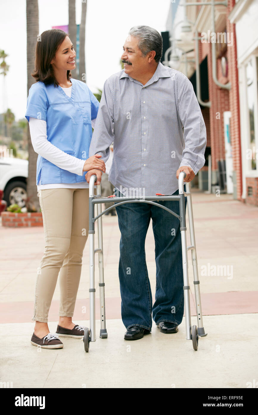 Carer Helping Senior Man To Use Walking Frame Stock Photo