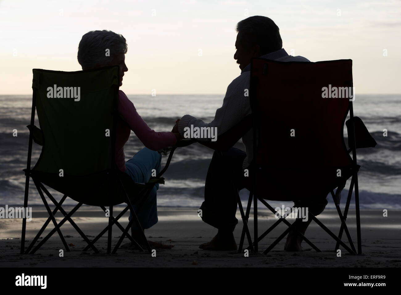 Silhouette Of Senior Couple Sitting On Beach In Deckchairs Stock Photo ...