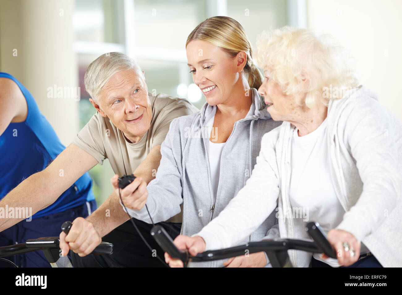 Fitness trainer measuring time for senior people on spinning bikes in gym Stock Photo