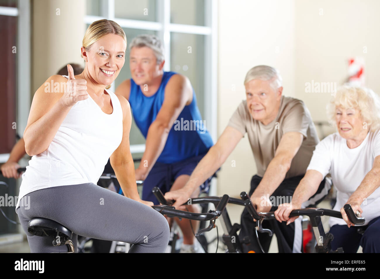 Happy fitness instructor in gym holding thumbs up with senior group ...
