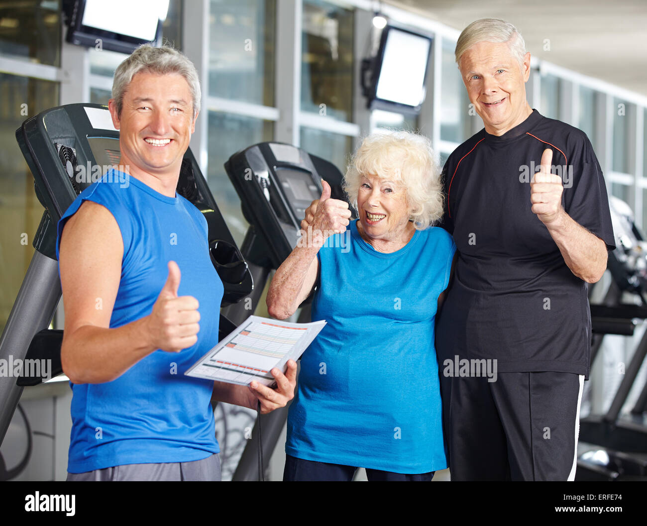 Happy senior couple in gym holding thumbs up with fitness trainer Stock ...