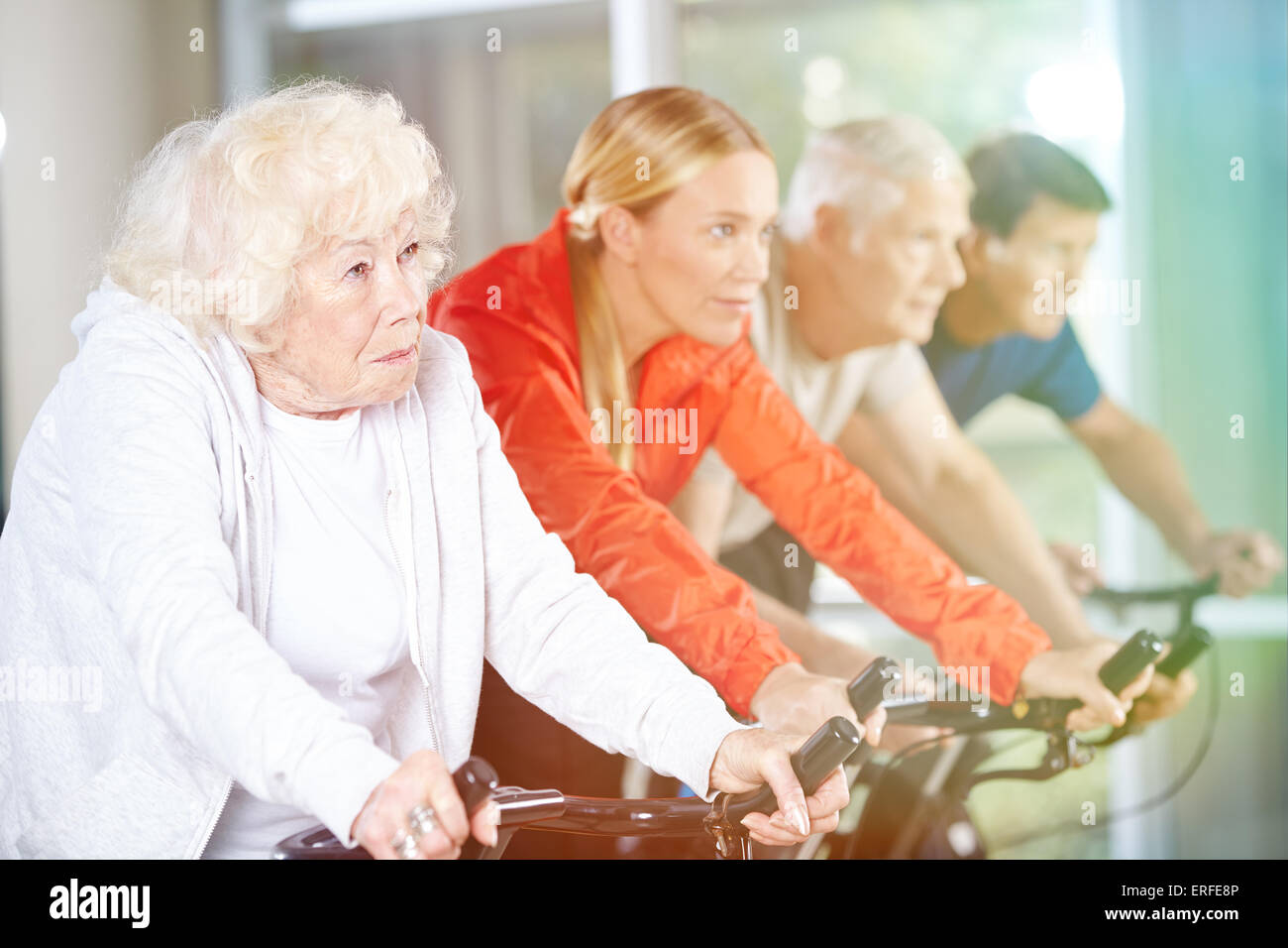 Old woman exercising in group on a spinning bike in gym Stock Photo