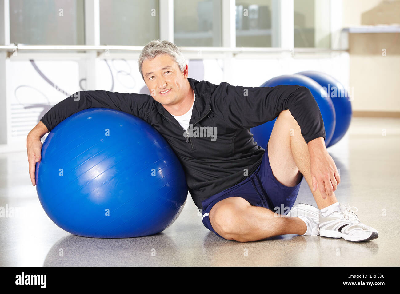 Happy senior man with gym ball in fitness center doing back training Stock Photo