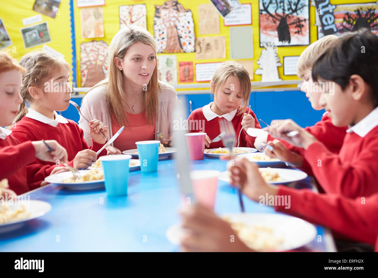 Schoolchildren With Teacher Sitting At Table Eating Lunch Stock Photo