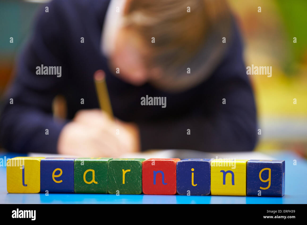 Word "Learning" Spelt In Wooden Blocks With Pupil Behind Stock Photo