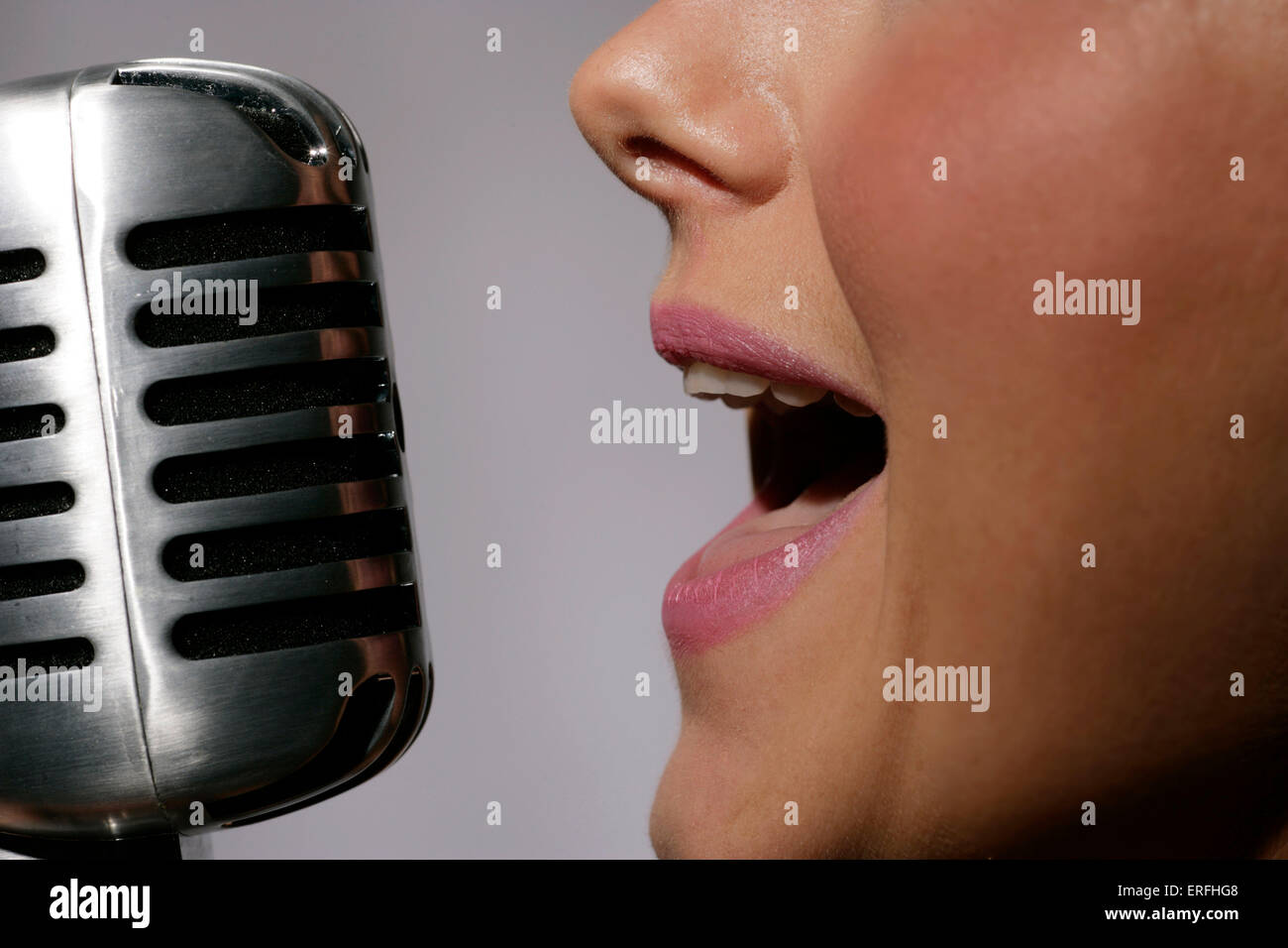 Microphone - a young woman singing in to a 50s 60s style microphone. Stock Photo