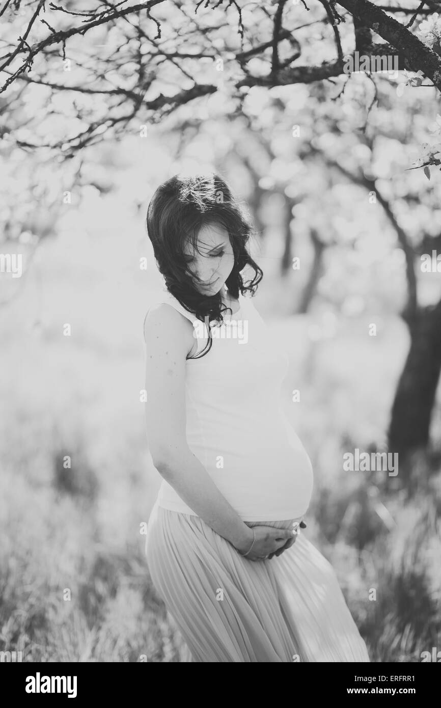 Young happy woman in expectation of baby. Female hands holding pregnant belly. Beautiful mother enjoying nature. Close up of pre Stock Photo