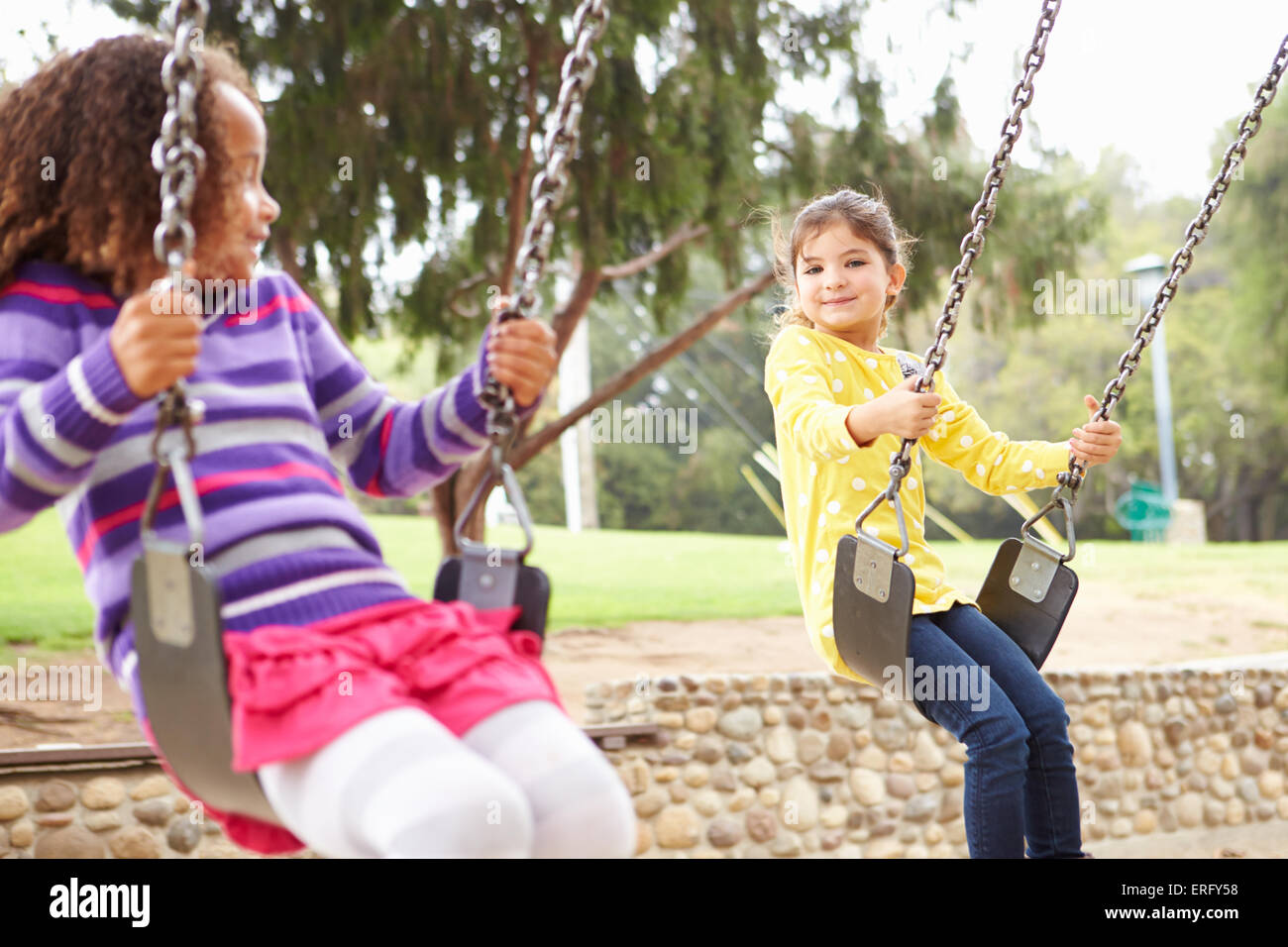 Two Young Girls Playing On Swing In Playground Stock Photo - Alamy