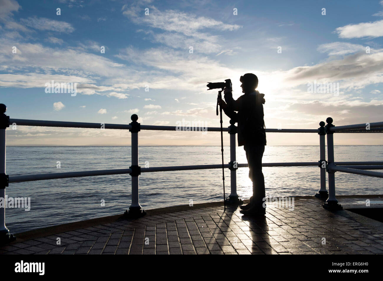 A keen amateur photographer at Penarth Pier in Cardiff taking a picture out to sea while using a monopod for camera support. Stock Photo