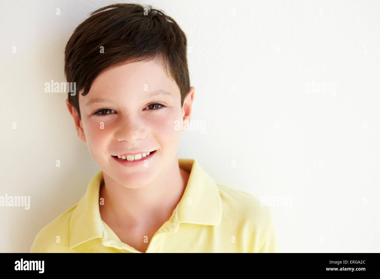 Smiling Young Boy Standing Outdoors Against White Wall Stock Photo