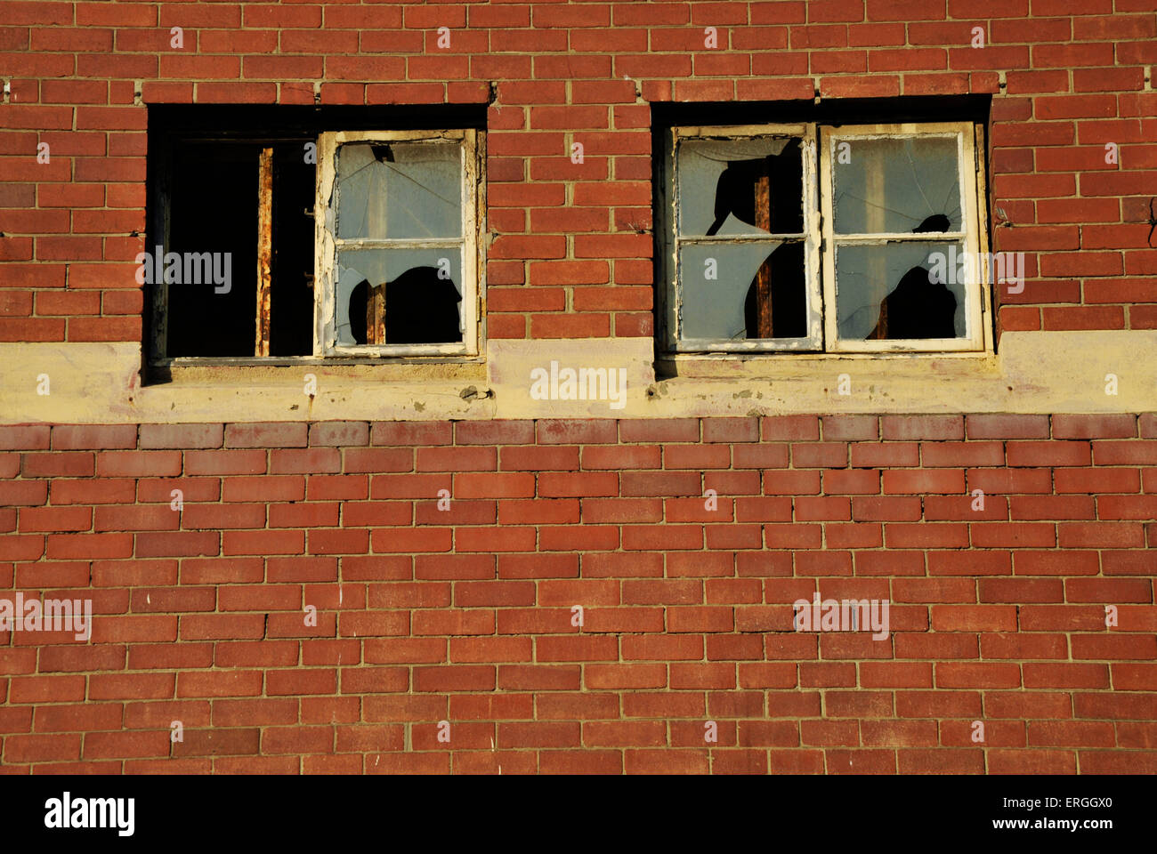 Two rusting window frames with broken glass in red brick wall of abandoned derelict old building Stock Photo