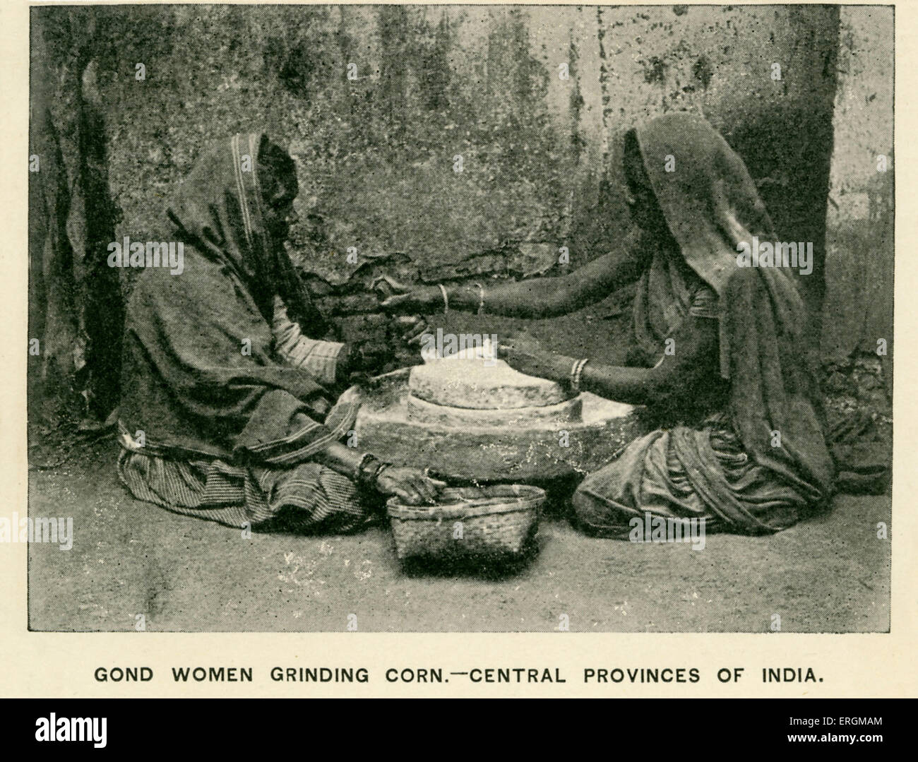Gondi women grinding corn. Photograph from early 20th century. The Gondi people are native to India's central states, with dense populations in Madhya Pradesh and Maharashtra. Adjacent quotation reads: 'In my judgment, Christian missionaries have done more real and lasting good to the people of India than all other agencies combined. They have been the salt of the country, and the true saviours of the Empire', attributed to Sir A. Rivers Thompson, Governor of Bengal. Stock Photo