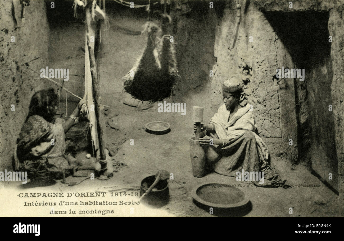 WWI Caption reads: Campagne d'Orient 1914 -1919. Interior of Serb home in the mountains. Two women weaving and pounding grains. Stock Photo