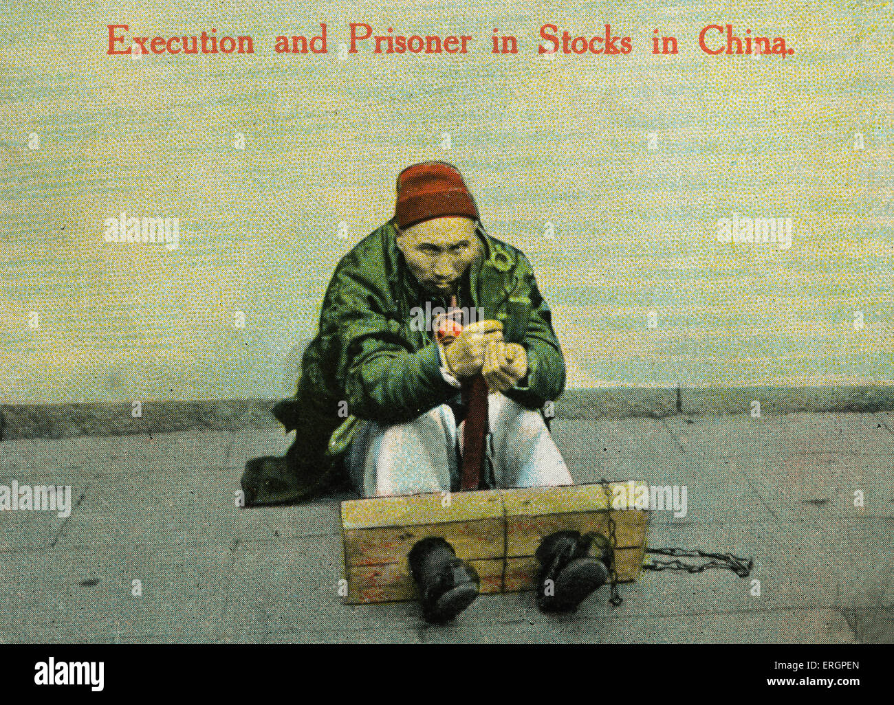 Male Muslim prisoner with  feet shackled to wooden stocks. China, early 20th century. Stock Photo