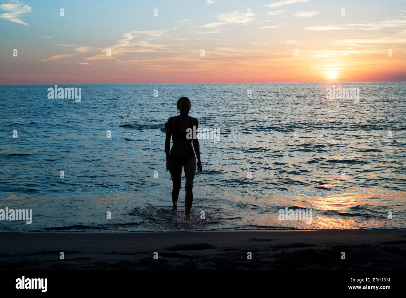 Beautiful girl silouhette coming out of the sea at sunset. Stock Photo