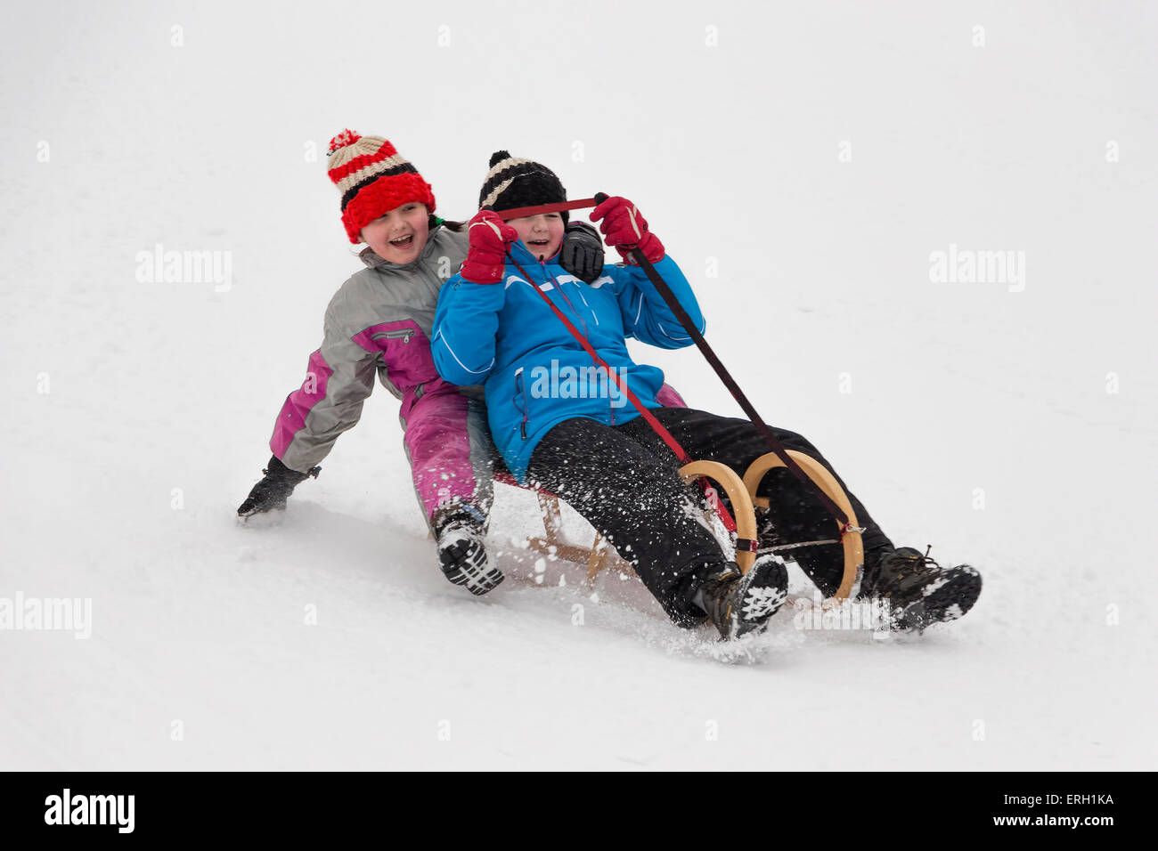 Two little girl in winter activity, sledging on wooden sledge downhill. Concept of winter activity enjoyed by children. Stock Photo