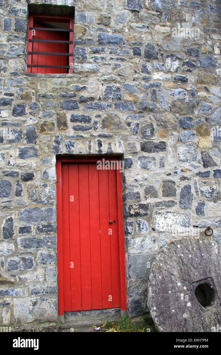 Beautiful old stone building with bright red wooden door and window, antique grinding stone set in front of building.. Stock Photo