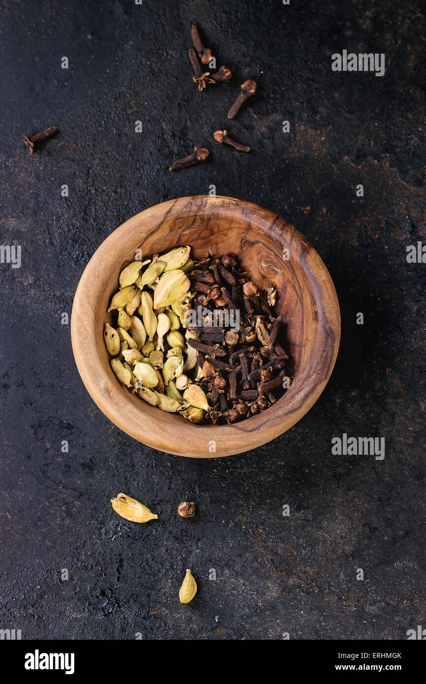 Cardamom seeds and cloves in olive wood bowl over black background. Top