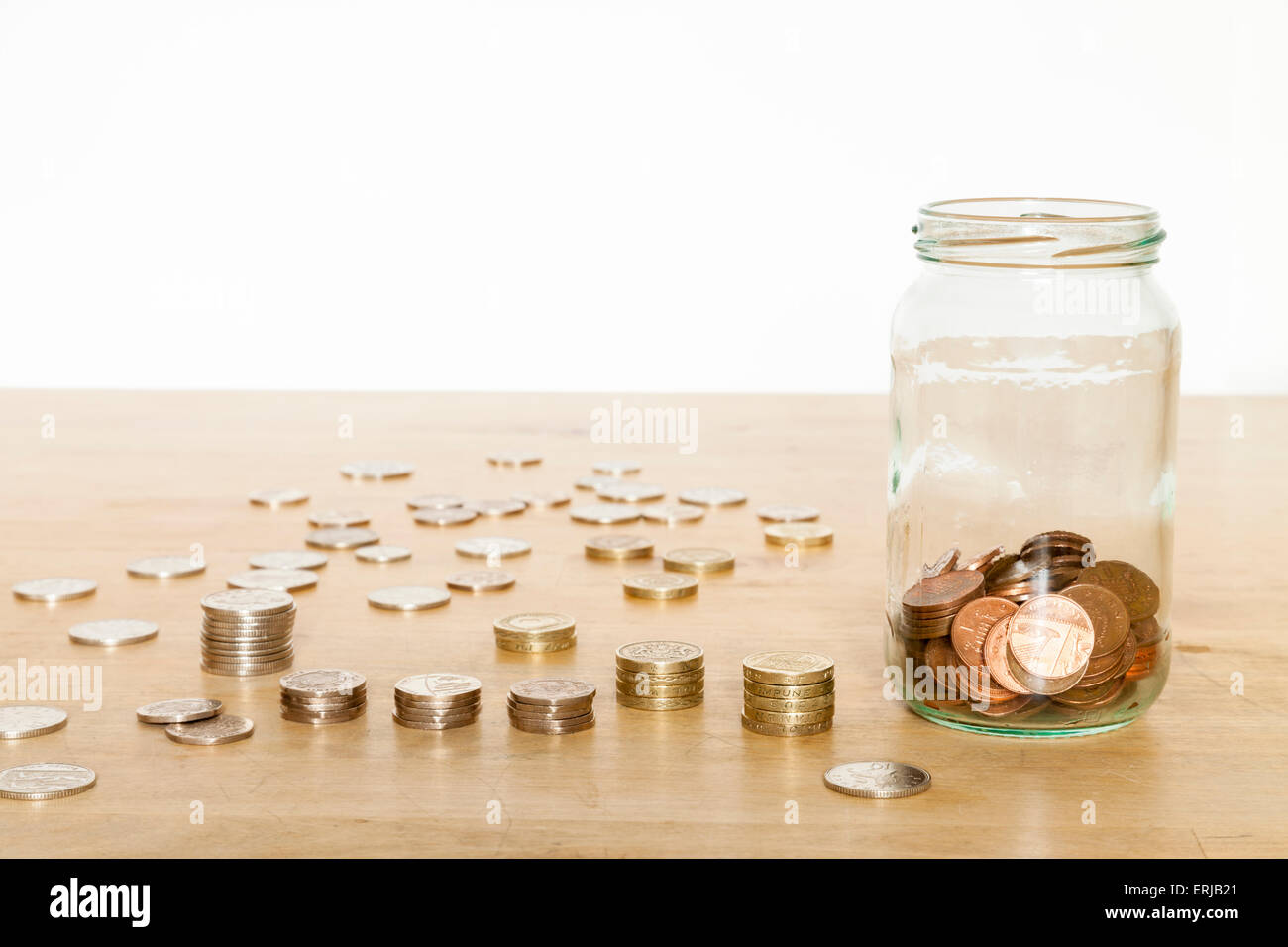 Cash savings jar. Saving money in a glass jar with UK coins stacked up and spread out on a table Stock Photo