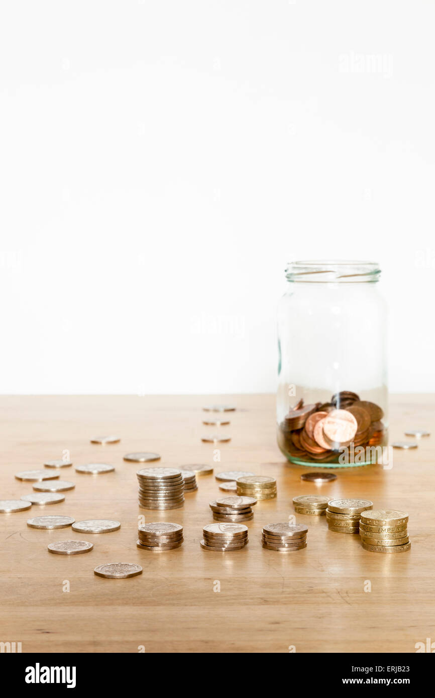 Cash savings jar. Saving money in a glass jar with UK coins stacked up and spread out on a table Stock Photo