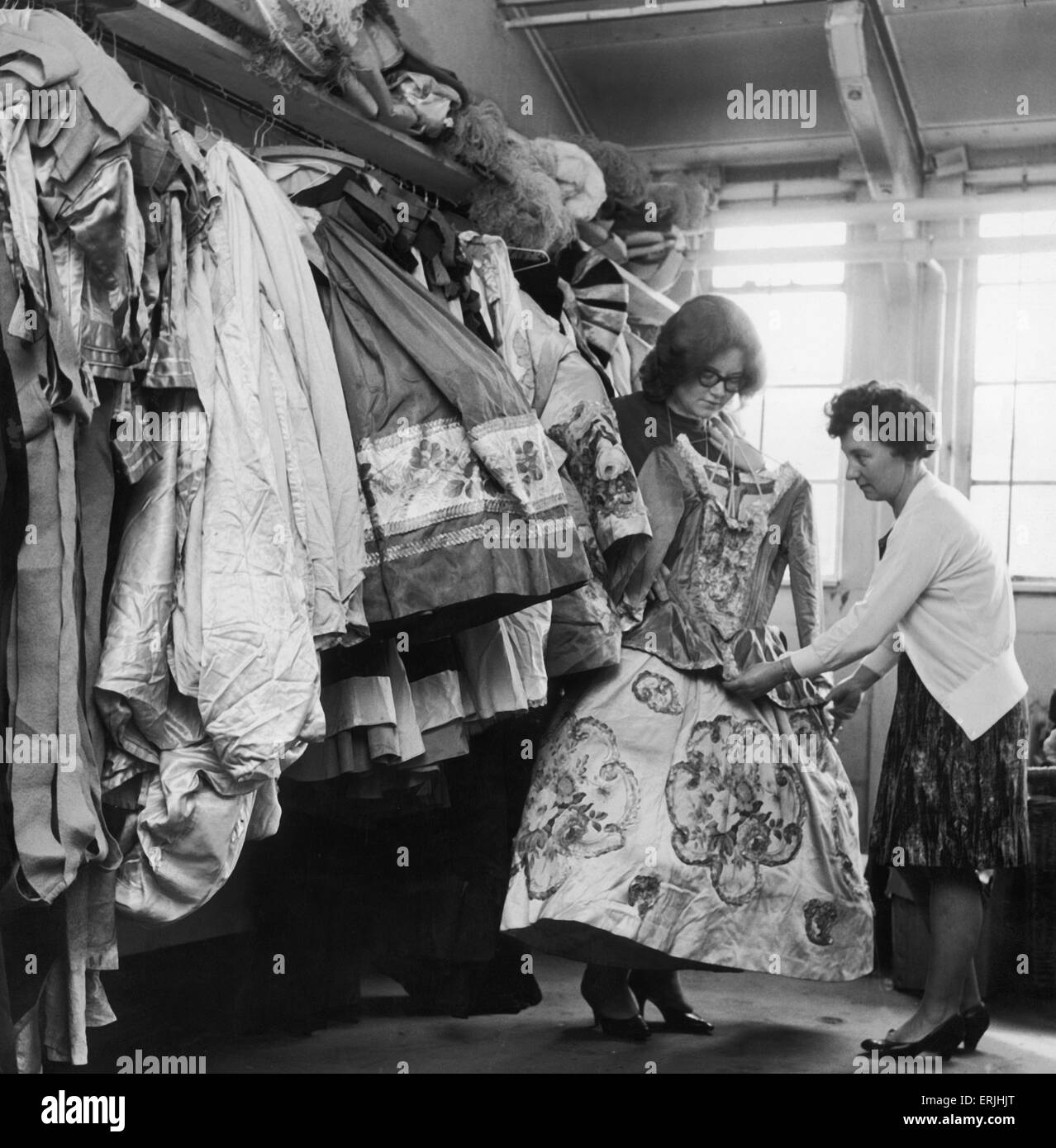 Miss Frances Roe wardrobe supervisor at the Coventry Theatre holds one of 10,000 costumes held by the wardrobe department, while her assistant Eunice Jenkins inspects the dress for damage. 9th October 1954 Stock Photo