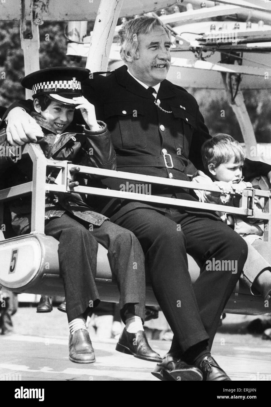 In safe hands of the law...Jason Lawson (left) aged 10 and Scott Marsdon aged 3, take a fairground ride with Superintendent Noel Edwards of Fletchamstead Police Station at the Coventry Memorial Park. Jason and Scott both of St Margaret's Special School, Bedworth were enjoying the offer of free rides for handicapped children which was made by Anthony Harris and Sons the fairs operator. 15th June 1979 Stock Photo