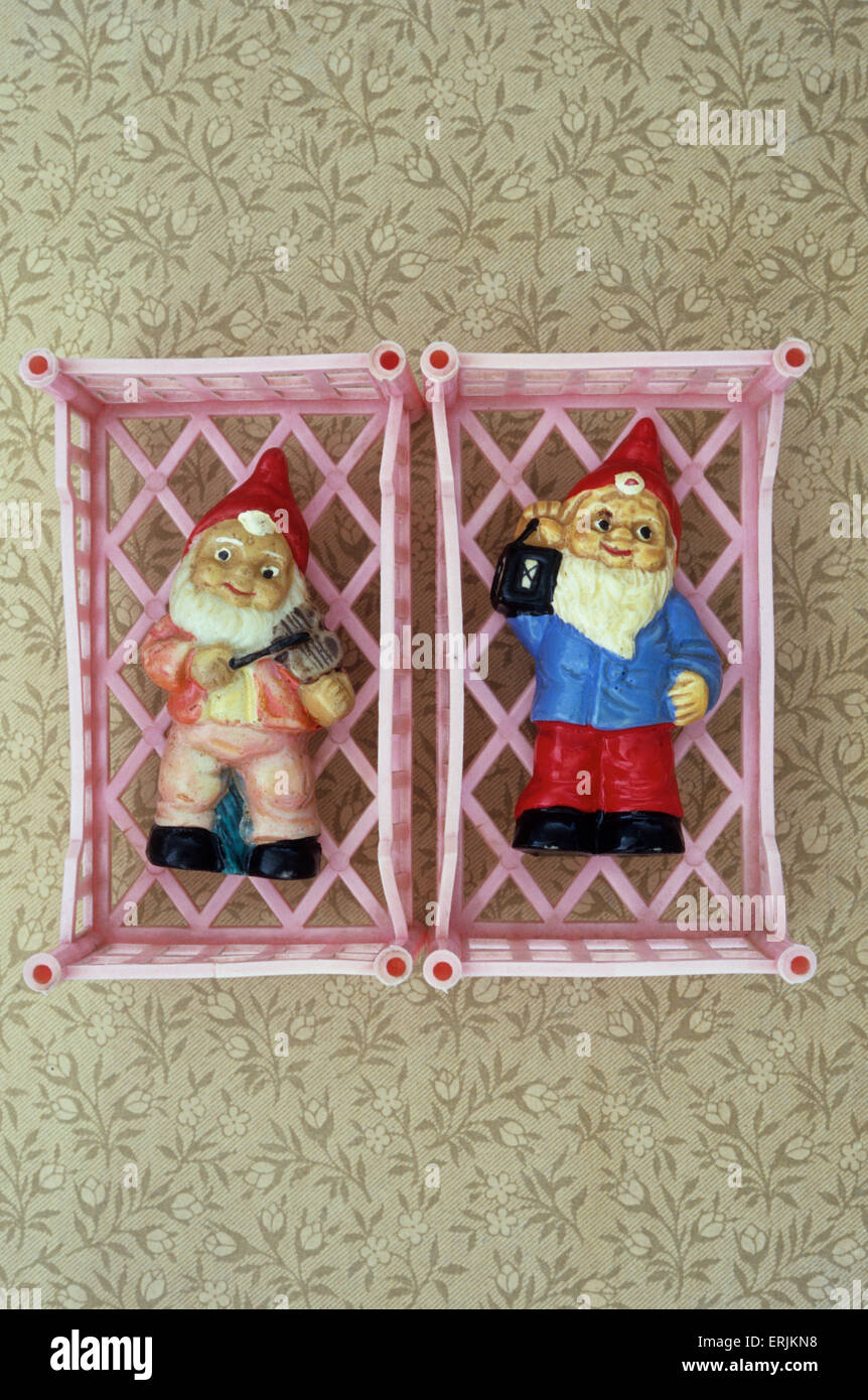 Two toy pink plastic cots on floral paper containing models of gnomes one with fiddle one with lantern Stock Photo