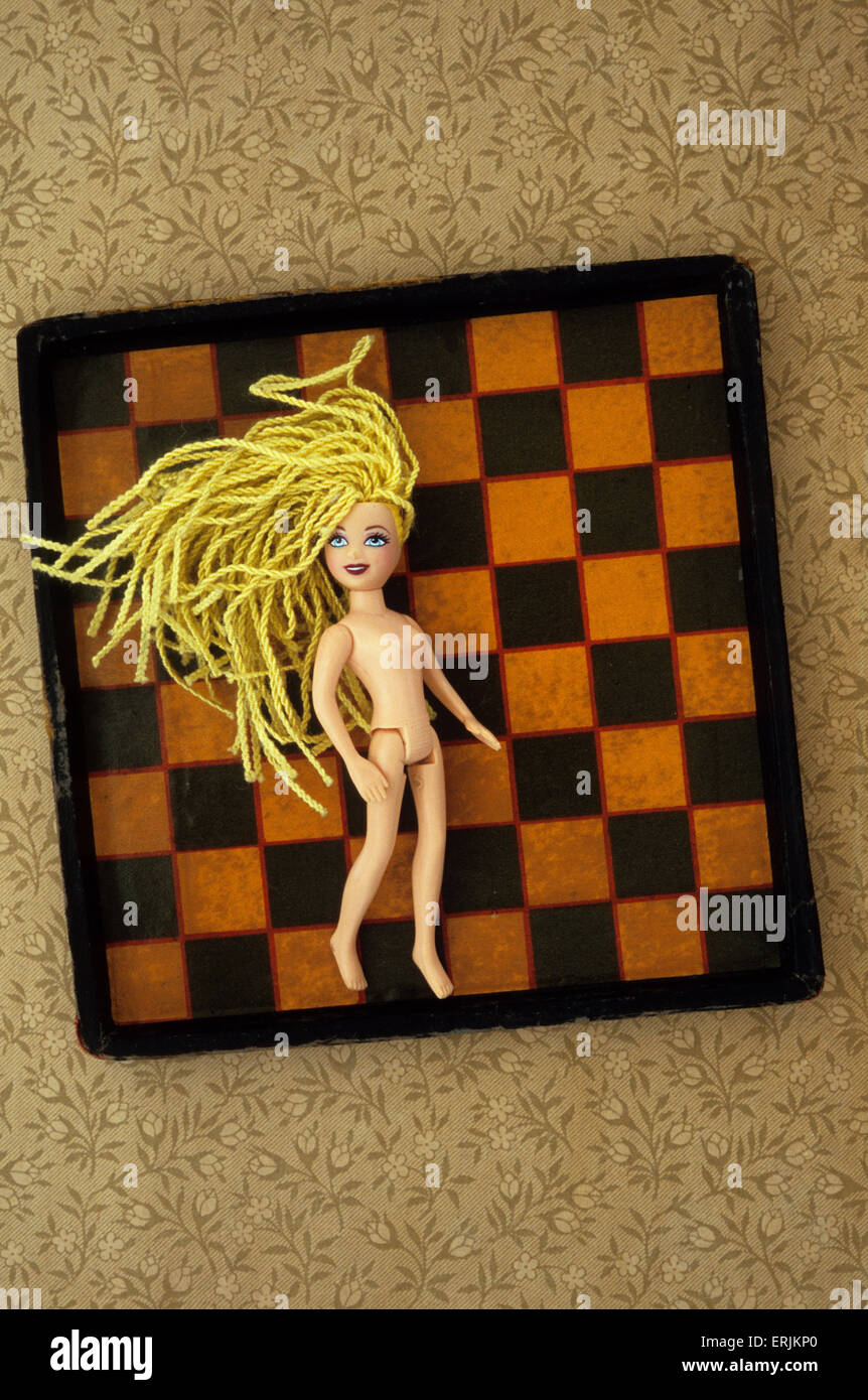 Plastic girl doll with stringy yellow hair lying on chess board Stock Photo