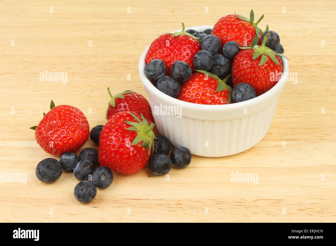 Strawberries and blueberries in and around a ramekin on a wooden board Stock Photo