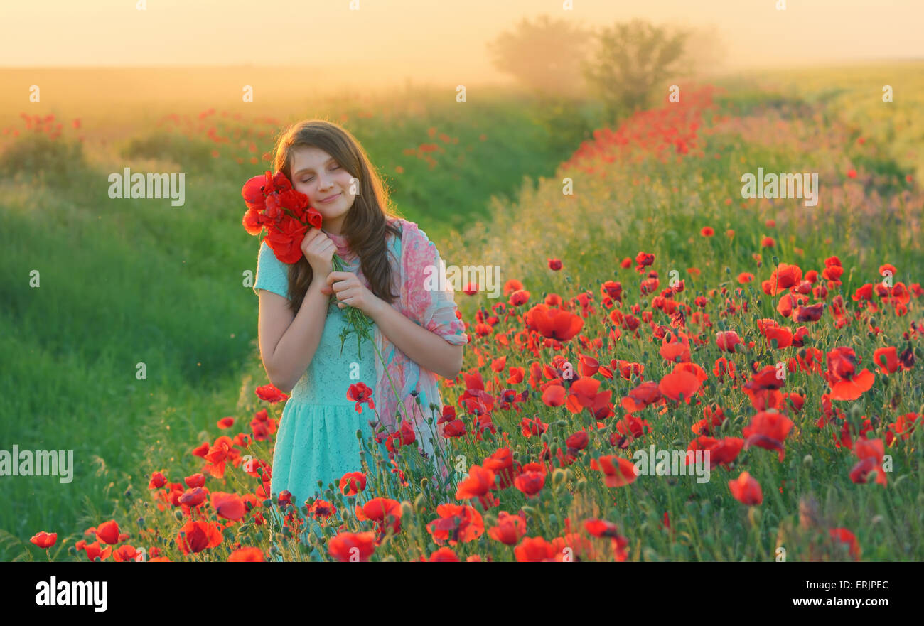 Girl stands in poppy field at sunset Stock Photo