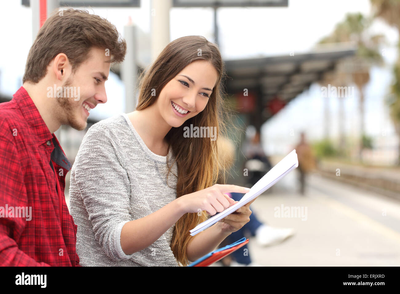 Happy couple of students studying and learning in a train station Stock Photo