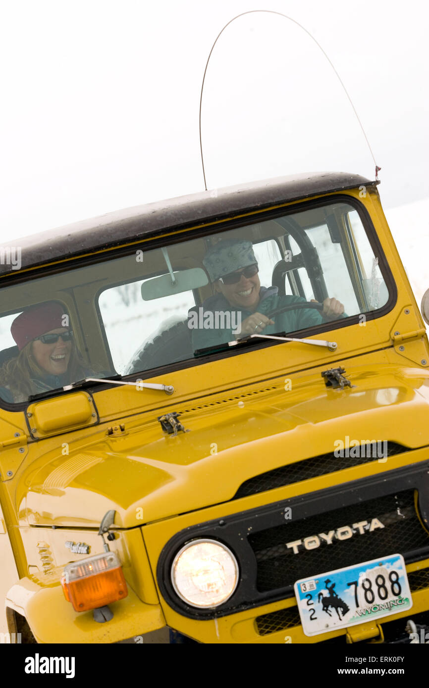 Two young women driving an old yellow landcruiser in the snow in Jackson, Wyoming. Stock Photo