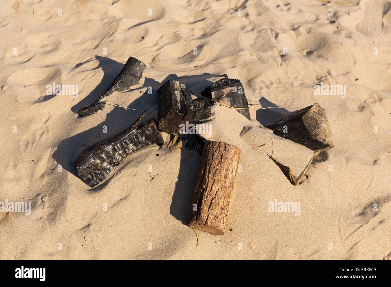 Remains of a small campfire with burned wood logs and sand on a beach Stock Photo
