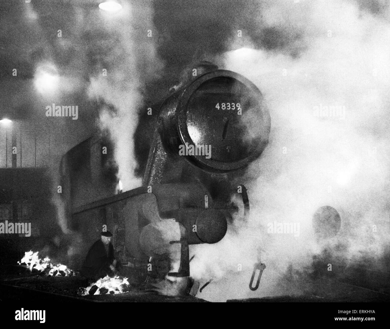 A London Midland & Scottish Railway  Class 8F- Stanier locomotive engine being de-iced by lighting coal fires around it at Saltley engine sheds. January 1963. Stock Photo