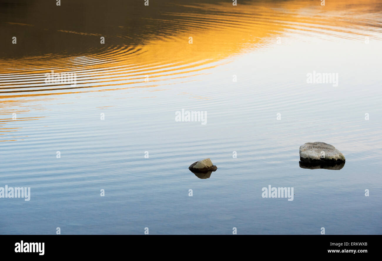 Dusk sunset reflections with stones and ripples on a Scottish loch Stock Photo