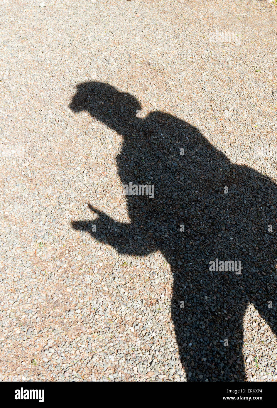 Shadow of a man wearing a brimmed hat in the sunlight pretending to point a gun with his fingers. UK Stock Photo